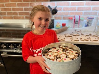 7 year old Cadence smiles at the camera in a Crisis t-shirt, holding a tin of homemade gingerbread men.