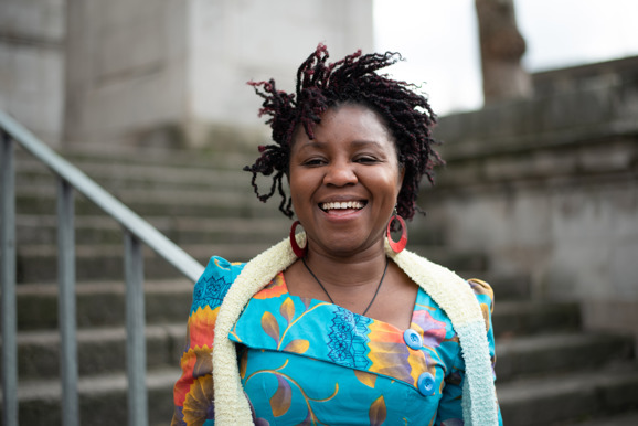 Smiling woman standing in front of outdoor staircase wearing colourful dress