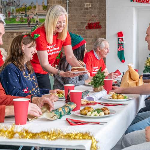 Con is celebrating at a Crisis dinner. Some of the attendees are wearing Crisis tshirts. Every one is smiling and wearing festive hats.