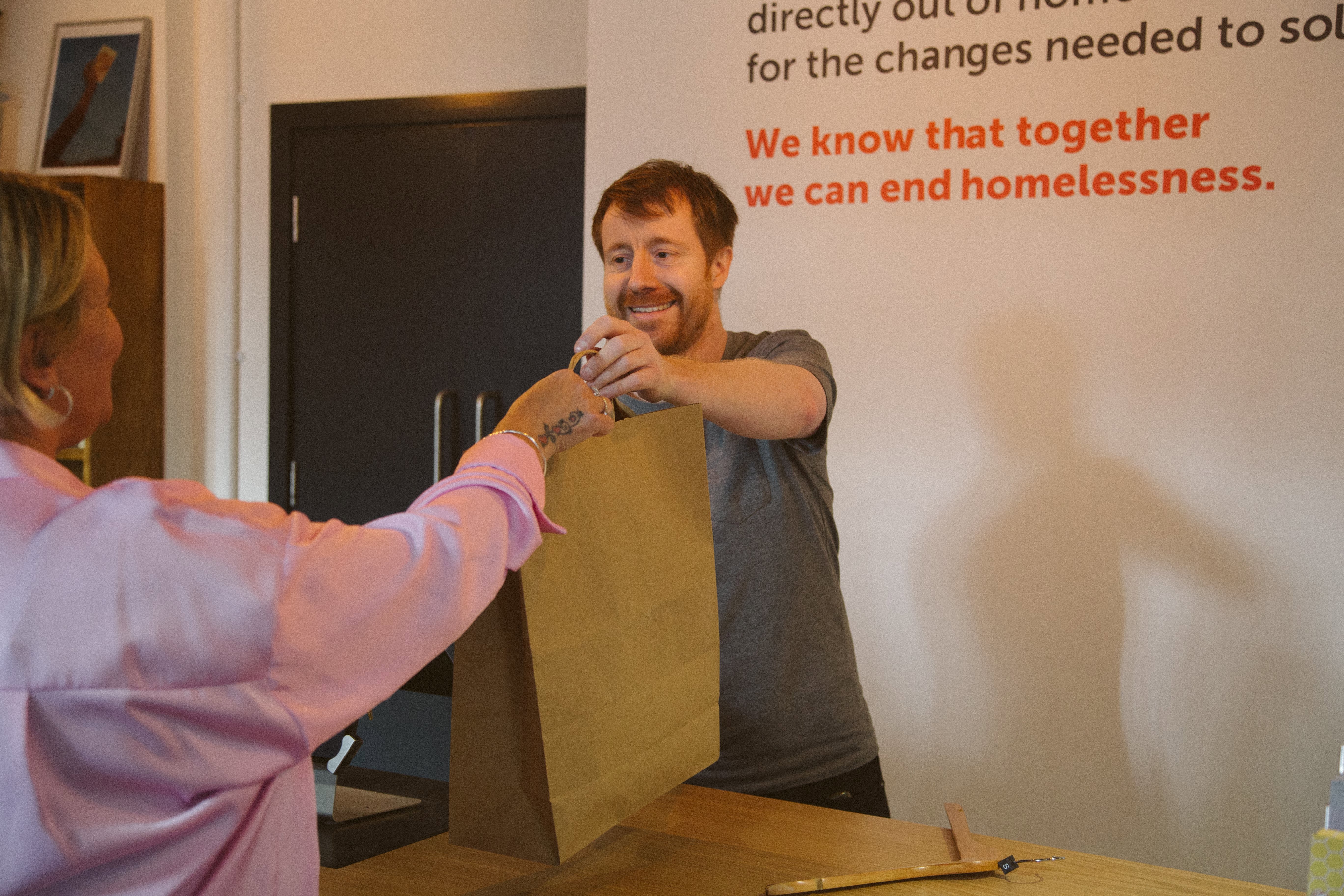 A volunteer hands a shopping bag to a customer in a Crisis shop