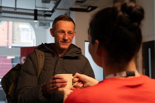 man in winter weather gear accepting a cup of tea from crisis staff member