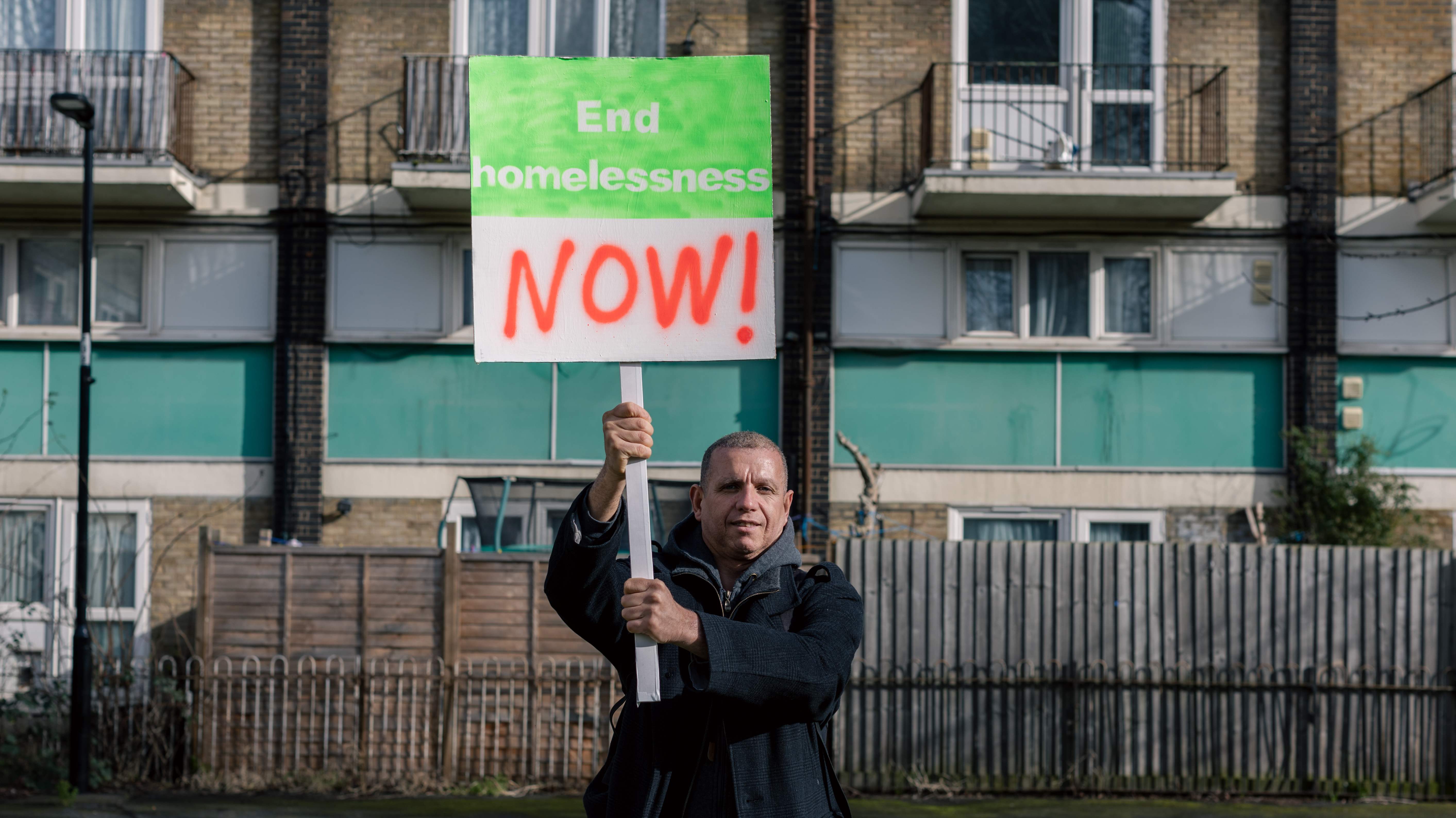 A hispanic man holding a placard that says 'end homelessness now!'